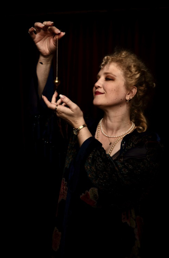 Krystyn Lambert reading a swinging pendulum before a dark velvet curtain