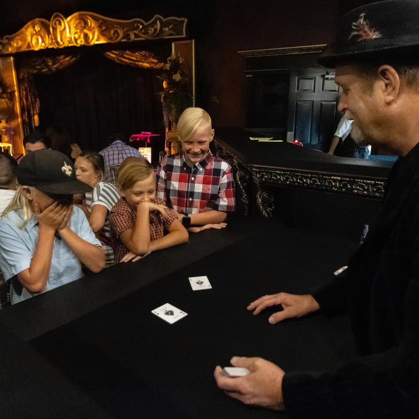 A magician performing a card effect at a guest table in the theatre