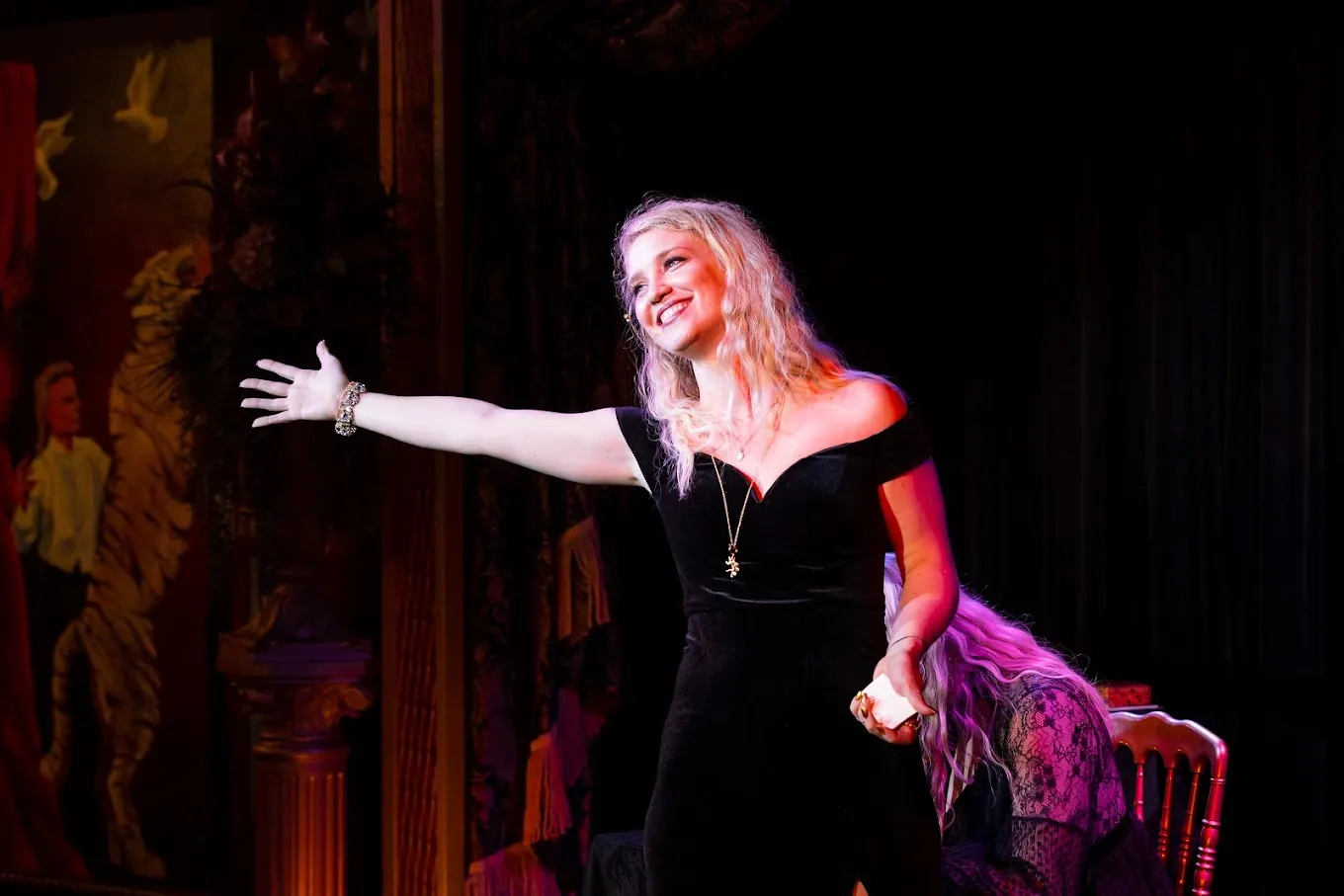 A magician mid-performance under warm stage light, arm outstretched to the audience