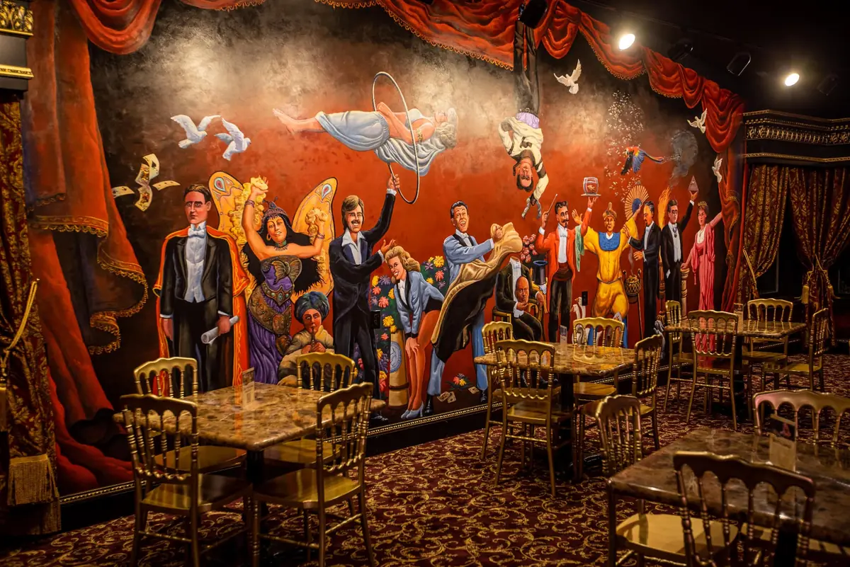 The hand-painted magicians' mural above marble tables and gilded chairs